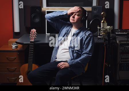 Trauriger Musiker, der seinen Kopf im Aufnahmestudio hält und seine Stimme verliert. Arbeitsplatz eines Tontechnikers in einem Tonstudio Stockfoto