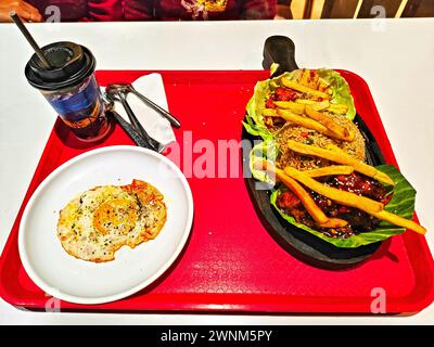 Bild eines Kombigerichts bestehend aus Eierpoach, sizzler und kalten Getränken, serviert auf einem roten Teller Stockfoto