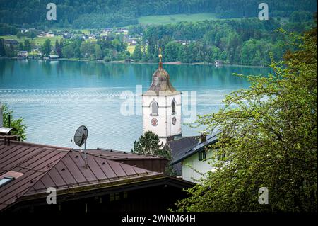 Blick über Dächer auf einen Kirchturm mit einem ruhigen See im Hintergrund, Sankt Wolfgang, Wolfgangsee, Salzkammergut, Österreich Stockfoto