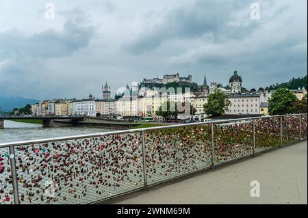 Eine Brücke mit vielen bunten Liebesschlössern am Geländer mit Blick auf die Stadt und Schloss im Hintergrund, Salzburg, Österreich Stockfoto