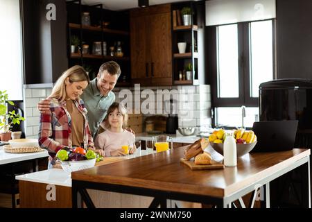 Die Familie teilt ein Lächeln, während sie gemeinsam das Frühstück in einer gemütlichen, gut beleuchteten Küche zubereitet Stockfoto