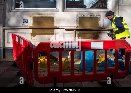 London, Großbritannien. 3. März 2024. Ein Bauarbeiter deckt die Slots für Geldautomaten und andere Einrichtungen in einer ehemaligen Filiale der NatWest Bank an der Chiswick High Road im Westen Londons ab. Da Banken hauptsächlich auf Online-Dienste umsteigen und physische Filialen schließen, um Geld zu sparen, sagen Kritiker, dass bestimmte Mitglieder der Gemeinschaft zurückgelassen werden, da sie auf Bargeld angewiesen sind, keinen Zugang zum Online-Banking haben und lieber direkten Kontakt mit Mitarbeitern ihrer lokalen Filiale haben. Quelle: Stephen Chung / Alamy Live News Stockfoto