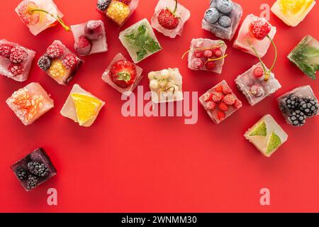 Roter Hintergrund mit Eiswürfeln mit gefrorenen Beeren und Früchten und Minze Stockfoto