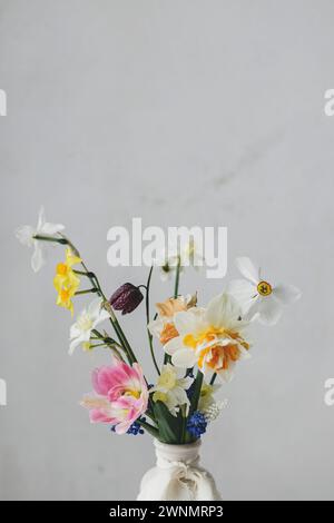 Stilvolle Frühlingsblumen in Vase mit Schleifenstillleben. Schöne Narzissen und Tulpen sanfte Bouquet. Leerzeichen für Text. Glücklicher Frauentag und Muttertag Stockfoto