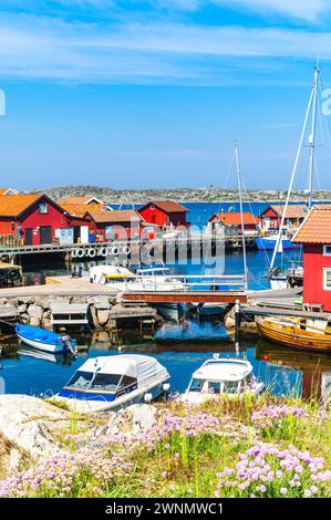 Im schwedischen Harbor entfaltet sich eine ruhige Szene, in der traditionelle rote Holzhäuser die Uferpromenade säumen. Vertäute Boote verschiedener Größen bewegen sich sanft in der Stockfoto