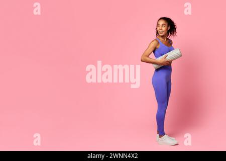 Athletische schwarze Dame mit Schaumstoffrolle, die auf rosa Hintergrund steht Stockfoto