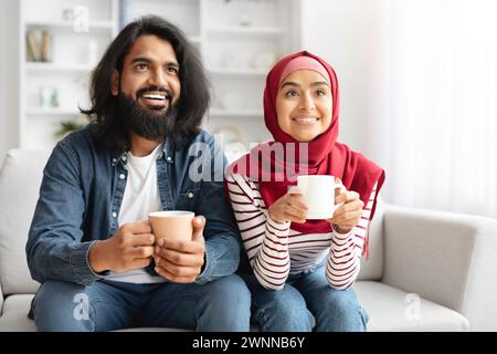 Glückliches Muslimisches Paar Trinkt Kaffee Und Entspannt Auf Der Couch Im Wohnzimmer Stockfoto
