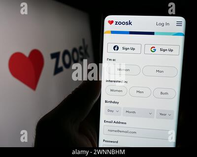 Person, die ein Handy mit dem Logo der Online-Dating-Plattform-Firma Zoosk Inc. Vor der Business-Website hält. Schwerpunkt auf dem Display des Telefons. Stockfoto