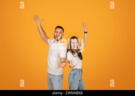 Fröhliche Männer und Frauen in weißen Oberteilen und blauen Jeans heben ihre Arme in einem verspielten Stockfoto