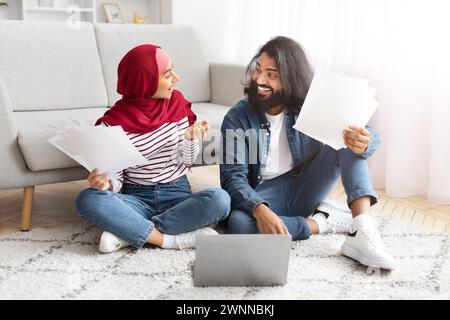 Muslimisches Paar Hält Papiere Und Plaudert, Während Er Zu Hause Auf Dem Boden Sitzt Stockfoto