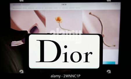 Person mit Smartphone und Logo des französischen Luxusmodeunternehmens Christian Dior SE vor der Website. Schwerpunkt auf dem Display des Telefons. Stockfoto