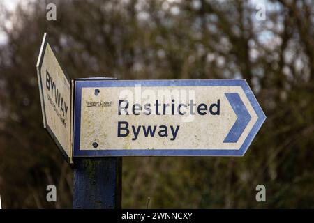 Restricted Byway Schild mit einem Pfeil nach rechts, vor einem verschwommenen Hintergrund von blattlosen Bäumen Stockfoto