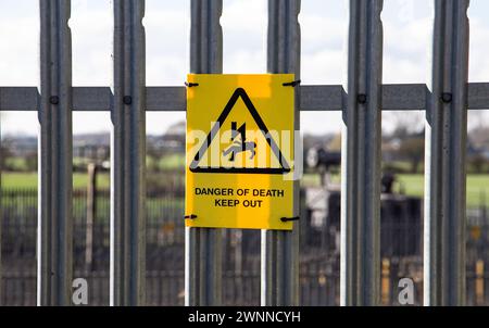 Warnzeichen für Stromschlaggefahr an einem Metallzaun mit ländlichem Hintergrund Stockfoto