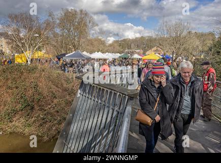 Käufer überqueren am 3. März 2024 die Fußgängerbrücke mit Marktständen im Hintergrund auf dem Frome Independent Sunday Market, Somerset, Großbritannien Stockfoto