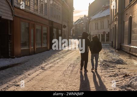 Zwei unbekannte Menschen laufen am frühen Morgen durch die verschneiten Straßen von bergen, hinterleuchtete Menschen, die einen langen Schatten auf die Kamera werfen. Stockfoto