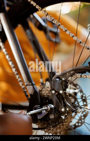 Nahaufnahme einer Person mit fachkundigen Arbeitsgeräten zum Einstellen und Sichern der Pedale und des Kettenrings. Detaillierte Aufnahme eines schwarzen Fahrradbauteils mit innensechskantschlüssel für die jährliche Wartung. Stockfoto