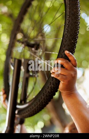Nahaufnahme eines weiblichen afroamerikanischen Handrads für die jährliche Sommerwartung im Freien. Gesunde Person, die Gummi auf Fahrradreifen im Heim befestigt und wechselt. Stockfoto