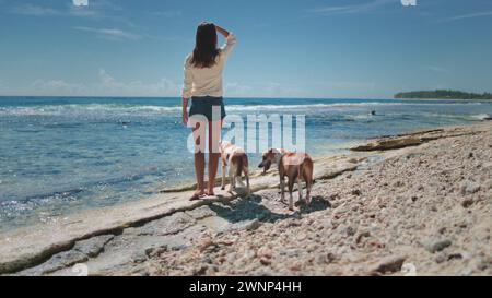 Frau geht mit zwei Hunden an der Strandküste. Frau genießt die Zeit mit ihren Haustieren, steht am Meer und am Meer. Echte Freundschaft, Sommerurlaub, Wochenendzeit, Relax. Freunde für immer. Rückansicht Stockfoto