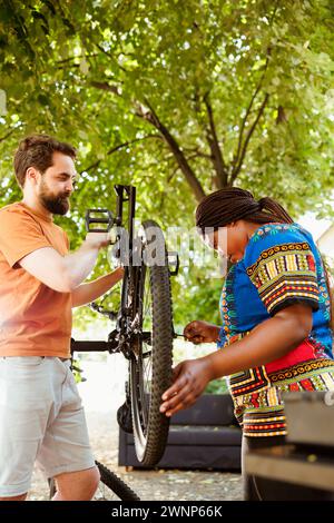 Sportliches multiethnisches Paar, das Radreifen und -Kette im Hof inspiziert und repariert. Gesunde und aktive zwei Personen arbeiten im Freien an der Fahrradwartung mit fachkundigem Arbeitsgerät. Stockfoto