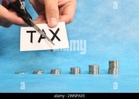 Steuersenkungskonzept. Hand schneidet Papier mit einer Schere auf blauem Hintergrund. Stockfoto