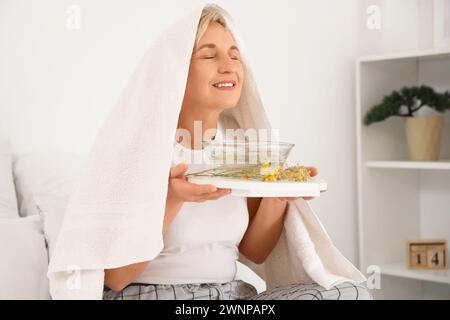 Reife Frau mit Handtuch, die im Schlafzimmer Dampf einatmet Stockfoto