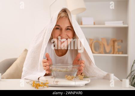 Reife Frau mit Handtuch, die im Schlafzimmer Dampf einatmet Stockfoto