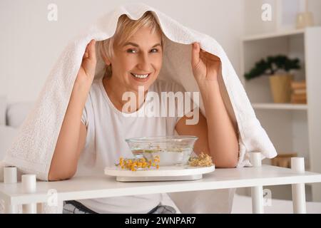 Reife Frau mit Handtuch, die im Schlafzimmer Dampf einatmet Stockfoto