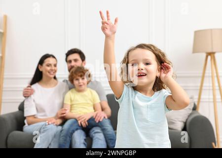 Glückliche Familie, die zu Hause Spaß hat. Tochter tanzt, während ihre Verwandten auf dem Sofa ruhen Stockfoto