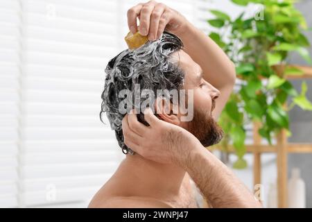 Mann wäscht sich die Haare mit einer festen Shampoo-Bar im Badezimmer, Nahaufnahme Stockfoto
