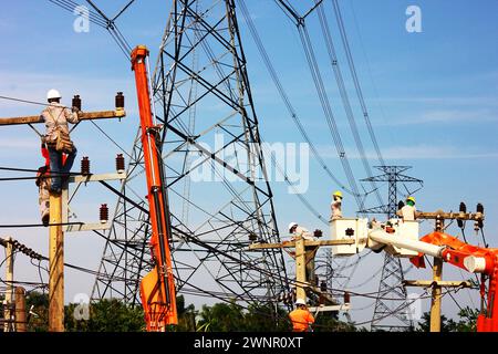 Gruppe von Elektroarbeitern, die an einem Pol angeschlossenen Hochspannungsdrähten unter einem Hochspannungspol arbeiten Stockfoto