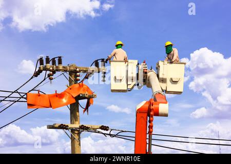 Elektrotechniker-Team, das an der Wiege der Hubplattform oder an einem Kran arbeitet, reparieren Hochspannungsleitungen vor blauem Himmel Stockfoto