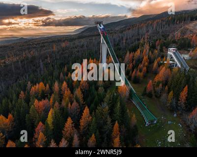 Strbske Pleso, Slowakei - aus der Vogelperspektive eine geschwungene Sprungrampe für Skispringen in der Hohen Tatra bei Strbske Pleso mit goldenen Wolken bei Sonnenuntergang und Colo Stockfoto