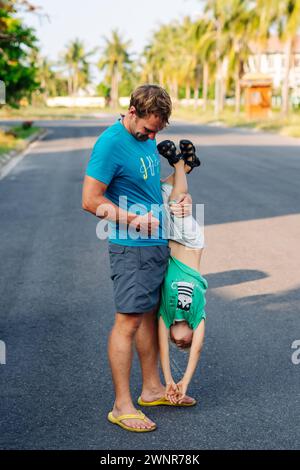 Vater Sohn, viel Spaß. Der Mann hält das Bein des Kindes auf dem Kopf. Freude Glück Kindheit Vaterschaft Freude Stockfoto