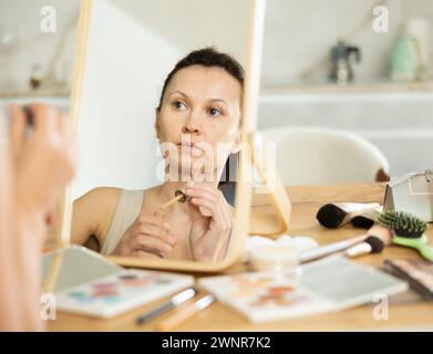 Frau mittleren Alters, die flüssige Foundation auf ihr Gesicht aufträgt Stockfoto