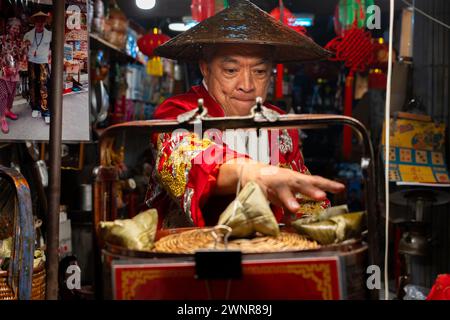 Thailand, 10. Februar 2024: Chakngeaw Chinese Village. Ein Verkäufer sucht nach einem Zongzi, einem klebrigen Reis mit herzhaften Füllungen in Bambusblättern. Stockfoto