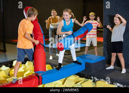 Glückliche Kinder Schuljunge und Teenager Mädchen kämpfen an aufblasbaren Baumstämmen, während sie ein Wochenende zusammen im Entertainment Center verbringen Stockfoto