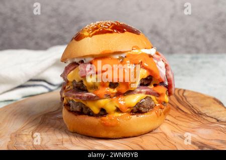 Doppel-Hamburger. Mit Cheddar-Käse, karamelisierten Zwiebeln, Roastbeef und Spezialsauce. Hamburger mit zwei Fleischbällchen auf Servierbrett. Nahaufnahme Stockfoto