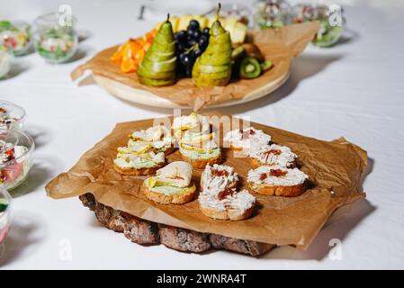 Eine vielfältige Auswahl an Bruschettas, großzügig mit verschiedenen Aufstrichen belegt, kunstvoll auf einer mit Pergament gesäumten rustikalen Präsentationstafel angeordnet. Stockfoto