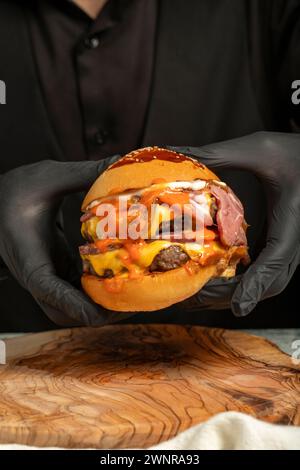 Doppel-Hamburger. Mit Cheddar-Käse, karamelisierten Zwiebeln, Roastbeef und Spezialsauce. Er hält einen Burger mit zwei Fleischbällchen in der Hand Stockfoto