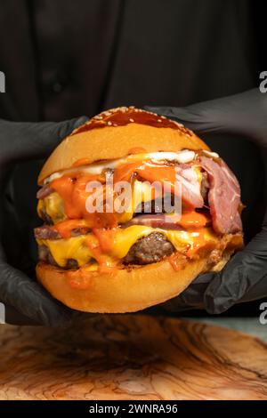 Doppel-Hamburger. Mit Cheddar-Käse, karamelisierten Zwiebeln, Roastbeef und Spezialsauce. Er hält einen Burger mit zwei Fleischbällchen in der Hand. Schließen Stockfoto