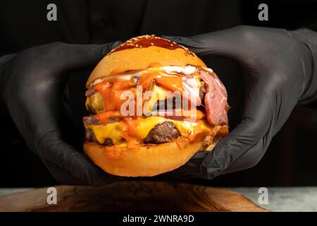 Doppel-Hamburger. Mit Cheddar-Käse, karamelisierten Zwiebeln, Roastbeef und Spezialsauce. Er hält einen Burger mit zwei Fleischbällchen in der Hand. Schließen Stockfoto