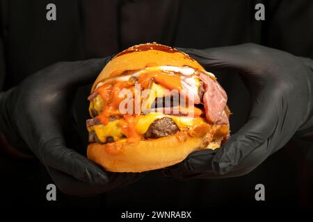 Doppel-Hamburger. Mit Cheddar-Käse, karamelisierten Zwiebeln, Roastbeef und Spezialsauce. Er hält einen Burger mit zwei Fleischbällchen in der Hand Stockfoto