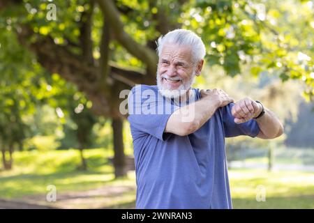 Ein älterer grauhaariger Mann verstauchte sich den Knöchel, während er im Park lief und Sport trieb, stand draußen und massierte seine Schulter mit der Hand und fühlte starke Schmerzen. Stockfoto