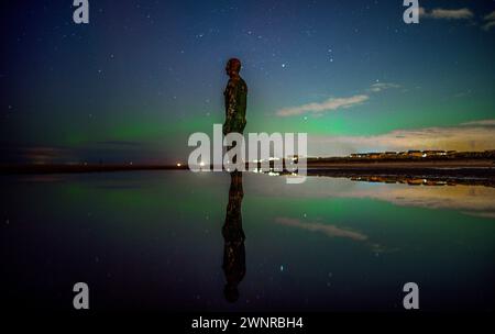 Die aurora Borealis, auch bekannt als die Nordlichter, sind über einer der Eisenmenschen Statuen an Anthony Gormley's Other Place, am Crosby Beach, Merseyside, zu sehen. Stockfoto