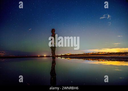 Die aurora Borealis, auch bekannt als die Nordlichter, sind über einer der Eisenmenschen Statuen an Anthony Gormley's Other Place, am Crosby Beach, Merseyside, zu sehen. Stockfoto