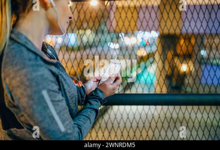 Läuferin, die den Bildschirm des Mobiltelefons mit Herzfrequenzmesser nach dem Training in der Stadt in der Nacht sieht Stockfoto