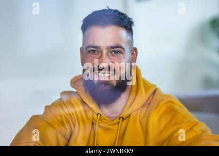 Ruhiger Mann in gelbem Sweatshirt, der in die Kamera schaut und lächelt. Stockfoto