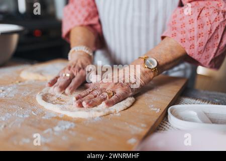Nahaufnahme der Hände einer älteren Frau, die traditionelle ostermahlzeiten für die Familie zubereitete, Teig für osterkreuzbrötchen kneten. Nachbildung von Familienrezepten Stockfoto