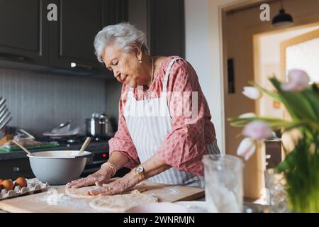 Seniorin, die traditionelle ostermahlzeiten für die Familie zubereitet, Teig für osterbrötchen kneten. Nachbildung von Familienrezepten, individuell. Stockfoto