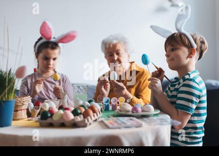 Großmutter mit kleinen Kindern, die ostereier zu Hause dekorieren. Tradition der Eiermalerei mit Pinsel und ostereifarbe. Stockfoto